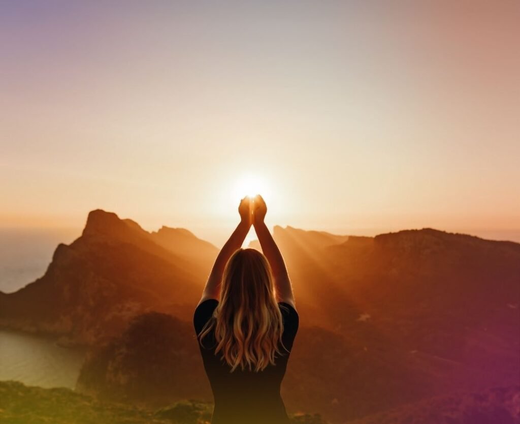 woman on a bluff looking over the rocks and water wtih her hands above her head welcoming the sun | When Empaths Awaken | The Vital Spirit | Laura Rowe | Empath Mentor