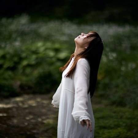 woman with dark hair standing in a field looking up wearing a white gown | When Empaths Awaken
